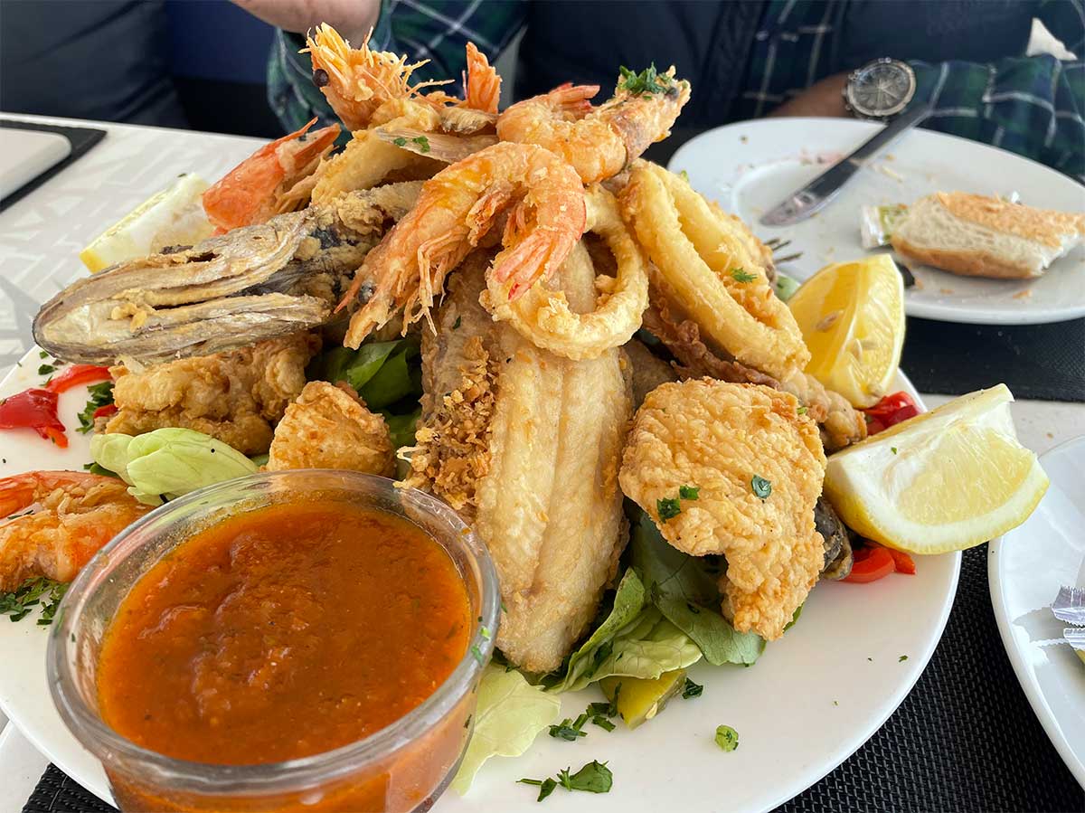 A plate piled high with fried fish, shrimp, and other seafood, accompanied by lemons and sauce