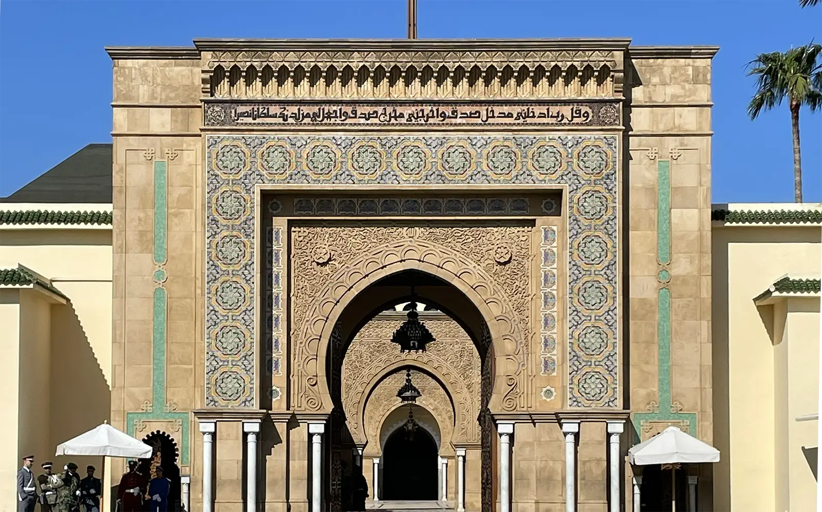 An elaborate stone palace gate with mosaic and with a red flag flying from the top