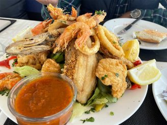 A plate piled high with fried fish, shrimp, and other seafood, accompanied by lemons and sauce